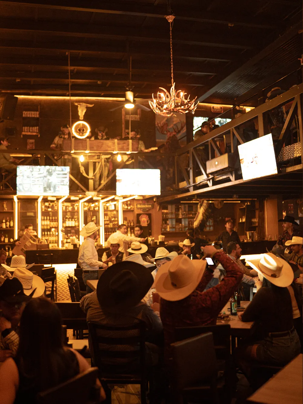 Salón de Cantina Del Desierto lleno, con candil de astas y sombreros vaqueros